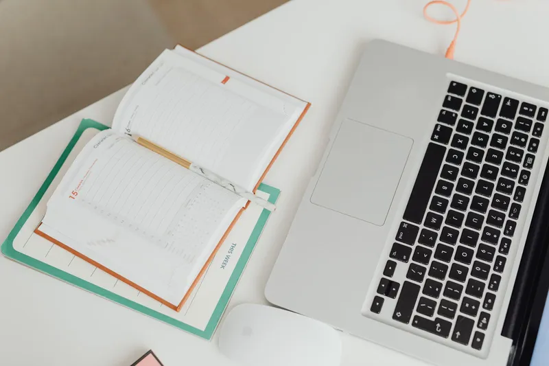 Top-down view of laptop and notebook planner on white desk
